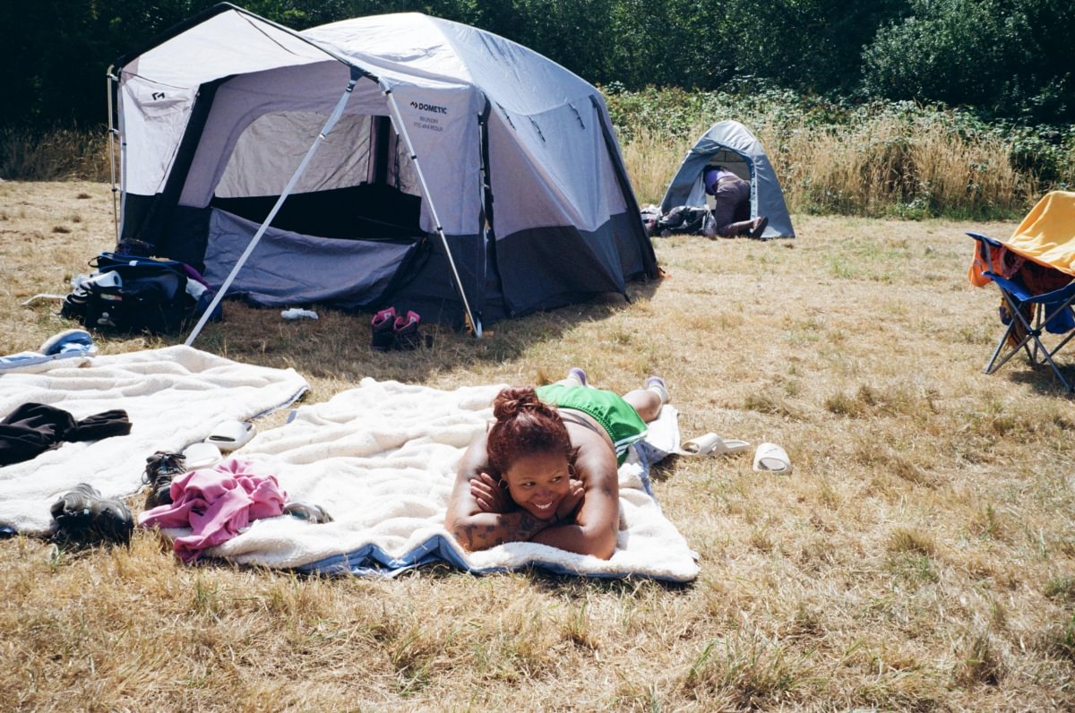 A person lying on a blanket on dry grass, outside a tent, in the sun