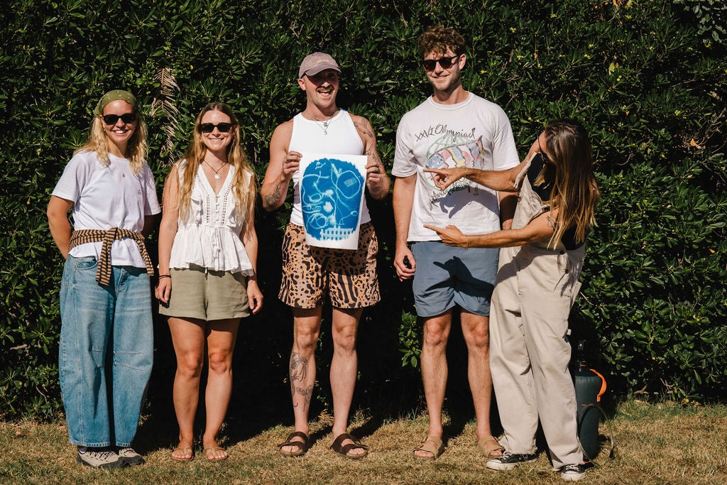 Five people smiling at the camera with a cyanotype piece of artwork being held by one man