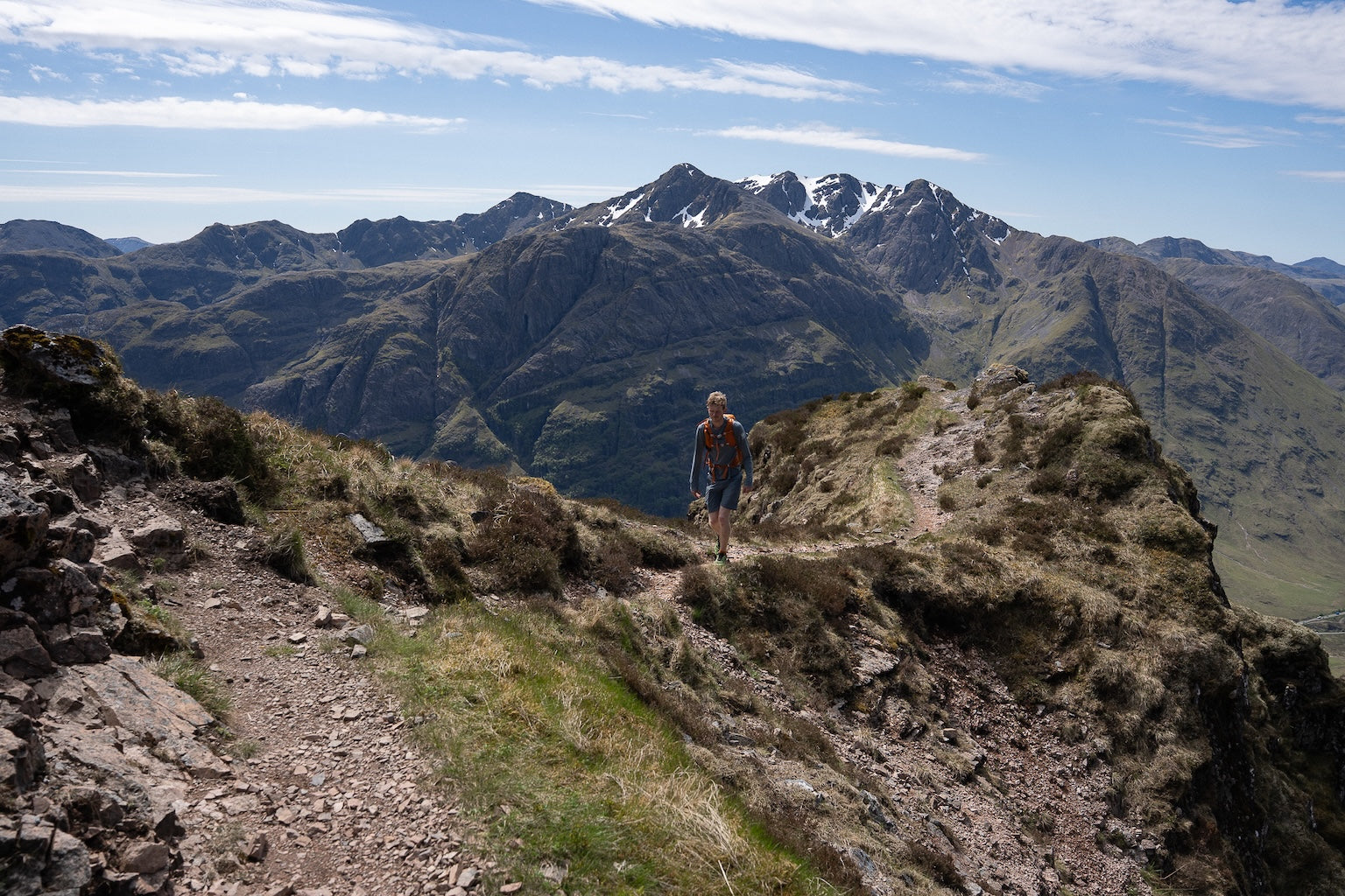 Person hiking on a mountain trail with snow-capped peaks in the background